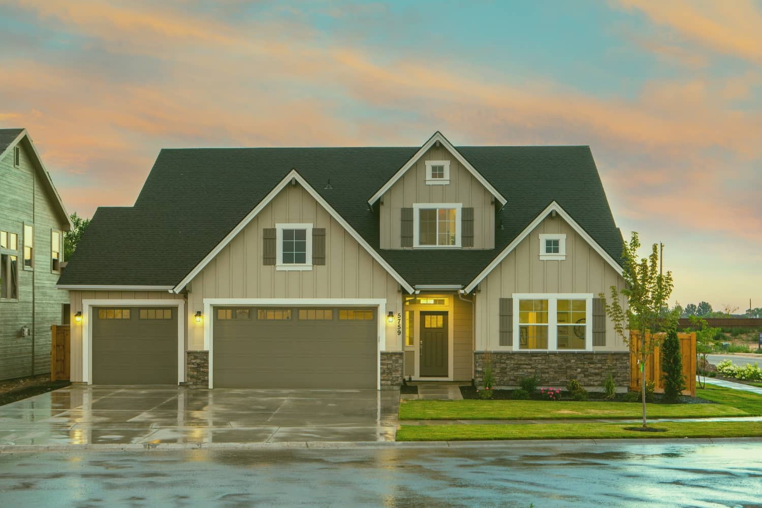 A modern two-story suburban home with tan siding, stone accents, and a two-car garage under a colorful twilight sky.