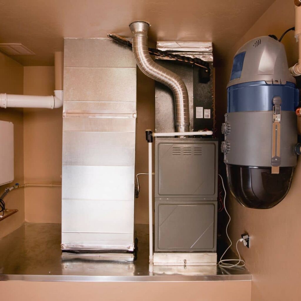Furnace in a utility closet with silver ductwork, a flexible exhaust vent pipe and a wall-mounted canister unit